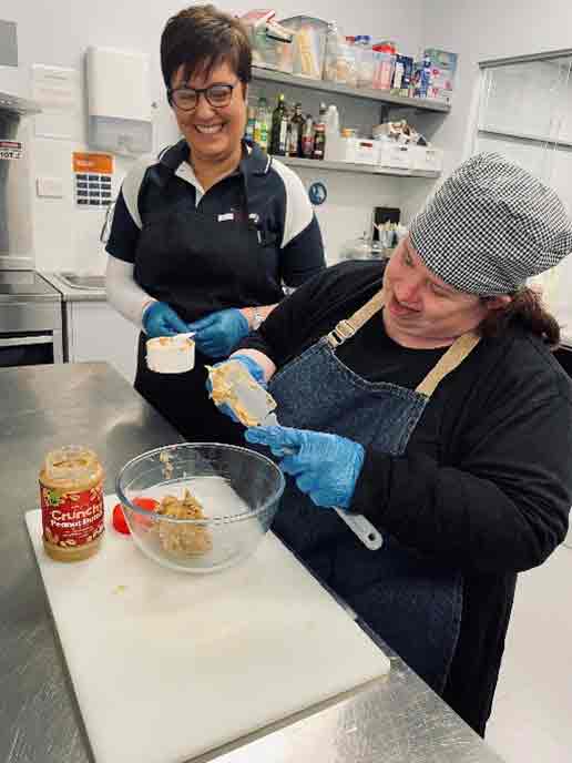 Two ladies in the kitchen using a rubber scraper with peanutbutter.