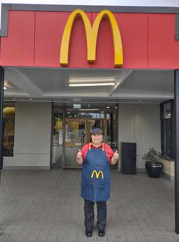 Man in McDonalds uniform in front of McDonalds building giving two thumbs up.