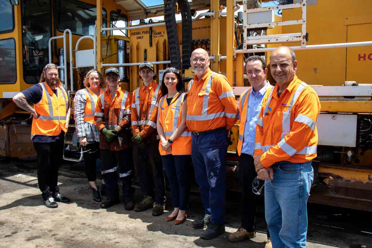 A group of people of varying ages wearing high vis and standing in front of a yellow train.