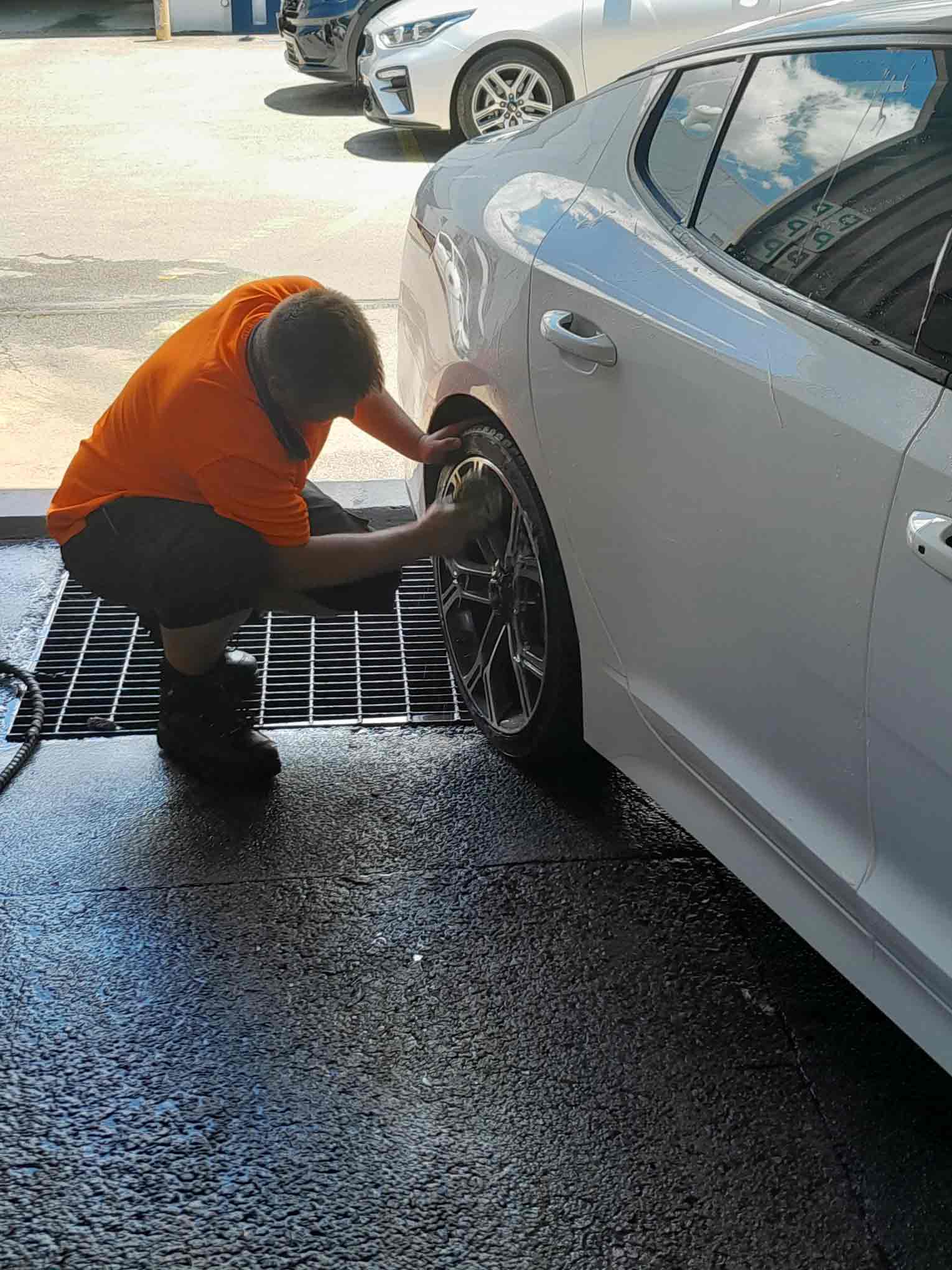 Man in High-Vis Shirt cleaning the rims of a car wheel. 