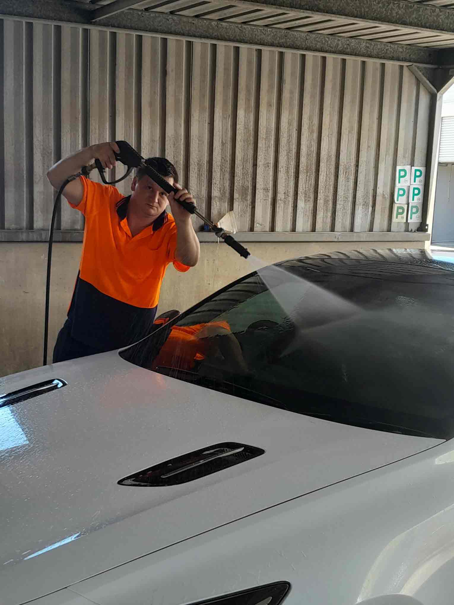 Man in High-Vis Shirt washing down car windscreen. 