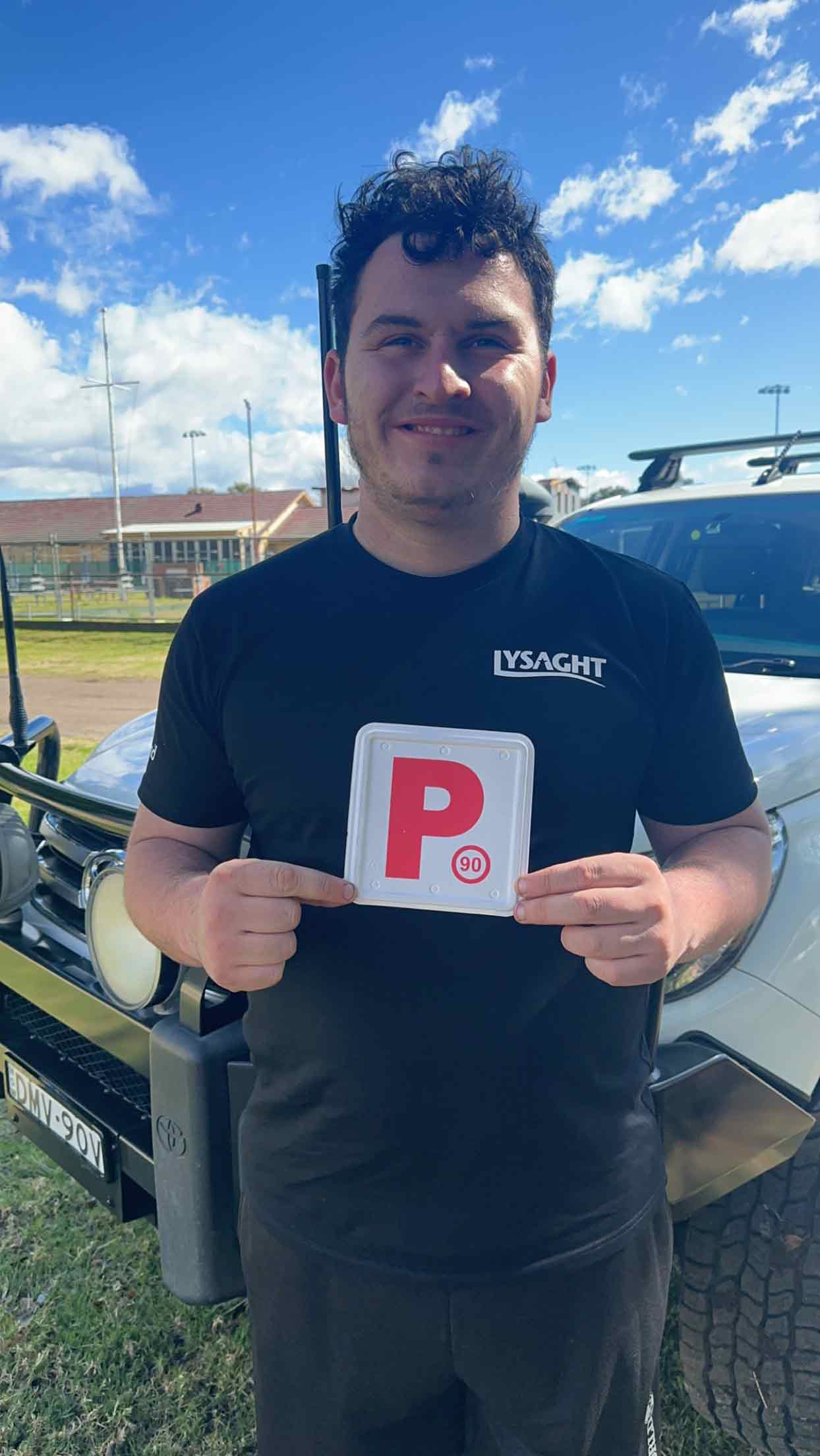 Young man holding his red P plates in front of a 4-wheel-drive.